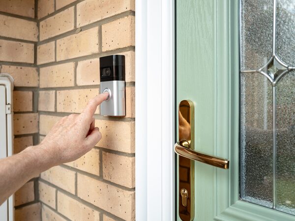 A finger pressing a video doorbell beside a front door